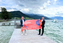 Erste Bojen-Verleihstation in Oberösterreich/Weyregg am Attersee eröffnet Zwei Männer halten orange Schwimmbojen und ein Plakat hoch, das den Ablauf des Ausleihens von Schwimmbojen erklärt. Sie stehen auf einem Steg am Attersee.