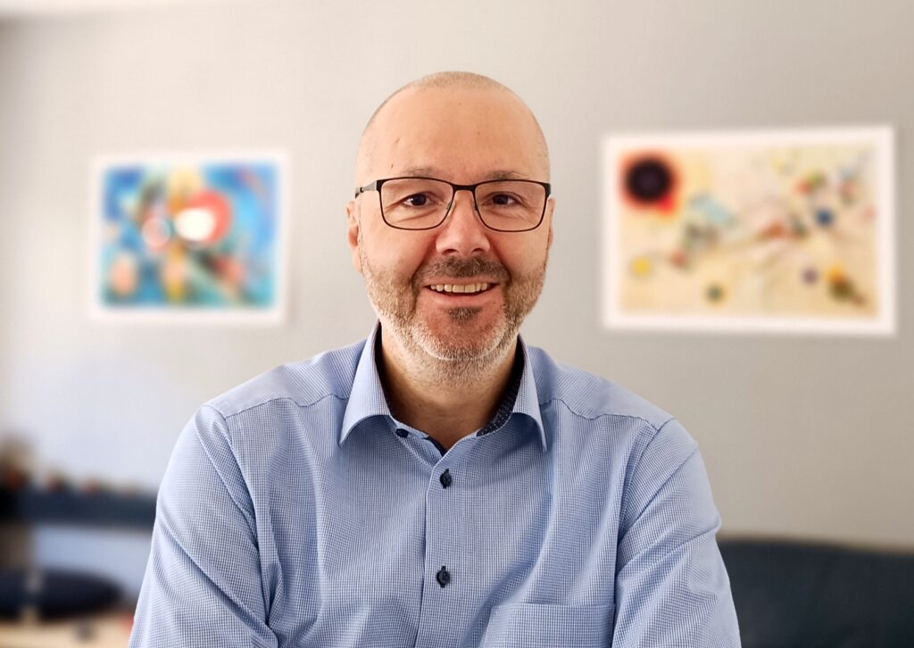 Alexios Wiklund, Sprecher des Österreichischen Tierschutzvereins, vor einer Wand mit bunten Natur-Bildern. Er trägt eine dunkle Brille und ein blaues Hemd und lächelt in die Kamera.