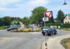 Drei dunkle Autos in einem Kreisverkehr. Davor ein Vorrang-Schild und der Hinweis "Blinken beim Verlassen".