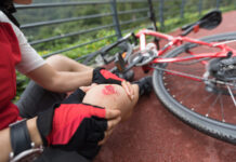 Ein Radfahrer mit einem aufgeschlagenen Knie und einem umgekippten Rad daneben.