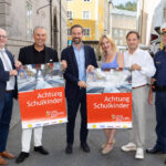 Sechs Personen, die zwei Plakate zu "Achtung Schulkinder" hochhalten für das Land Salzburg und in die Kamera lächeln.